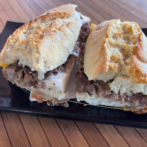 Un bocadillo de carne desmenuzada y queso fundido servido en un plato negro.