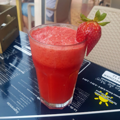 Vaso de batido de fresa con una fresa entera colocada en el borde del vaso, servido en una mesa de restaurante.